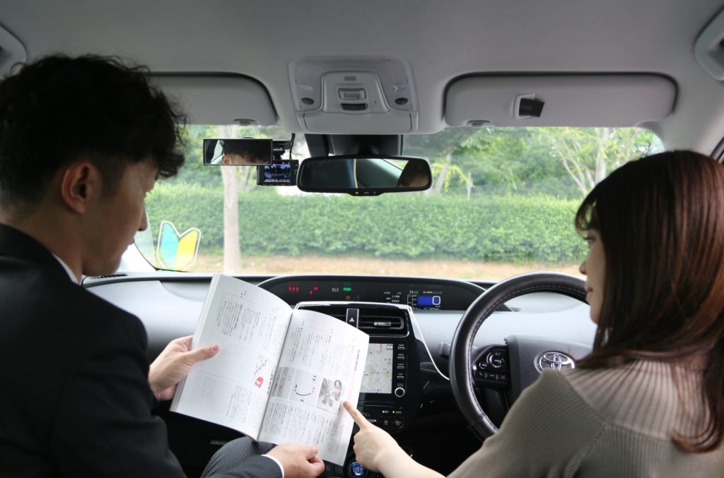 車内で教官が資料を見せながら説明している様子